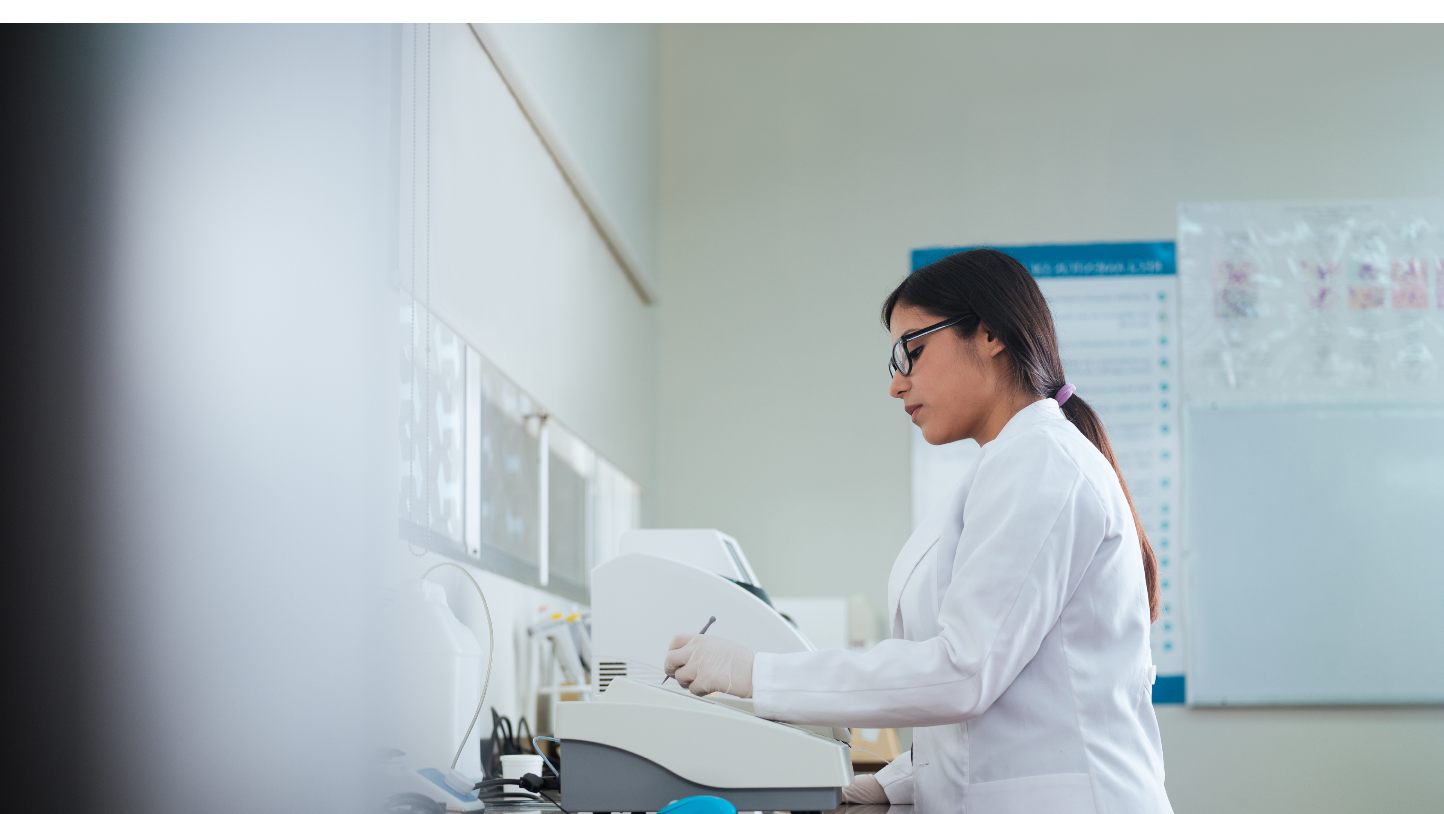 A latin female student in laboratory class, standing and using a device.